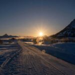 A beautiful winter sunset over a snowy mountain road, creating a tranquil and scenic view.