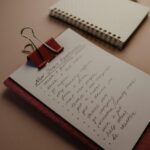 A flat lay of a clipboard with New Year’s resolutions and a notebook on a desk.