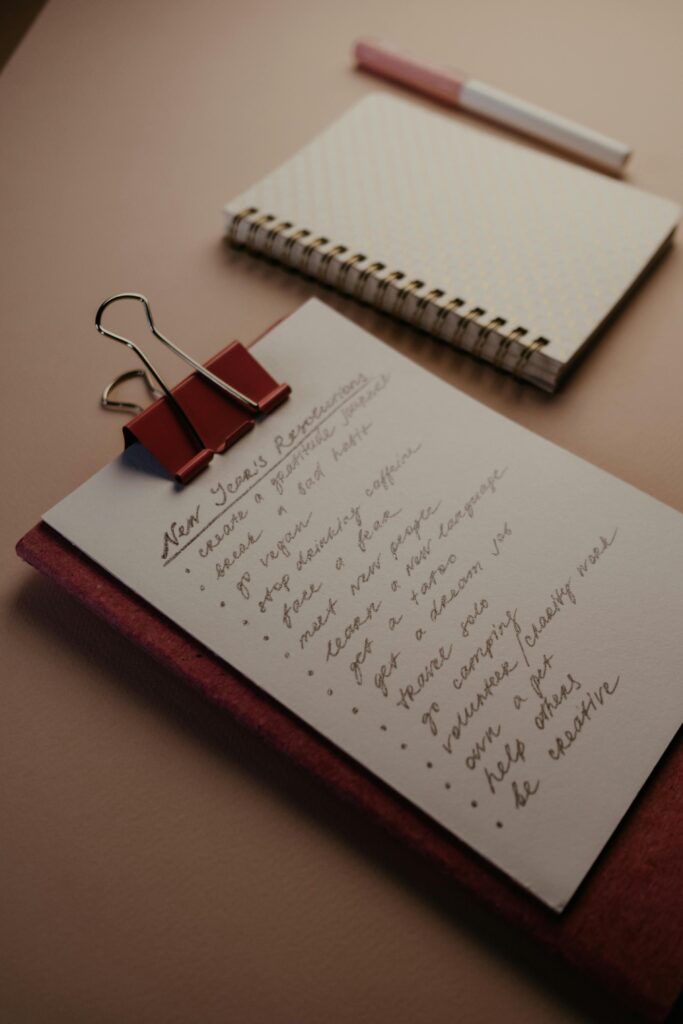 A flat lay of a clipboard with New Year’s resolutions and a notebook on a desk.