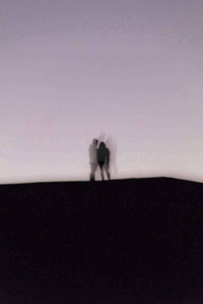 A blurry silhouette of a couple standing together against a twilight sky, creating a mysterious and dreamy effect.