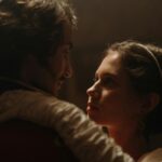 A couple in historical costumes sharing an intimate moment indoors with soft lighting.