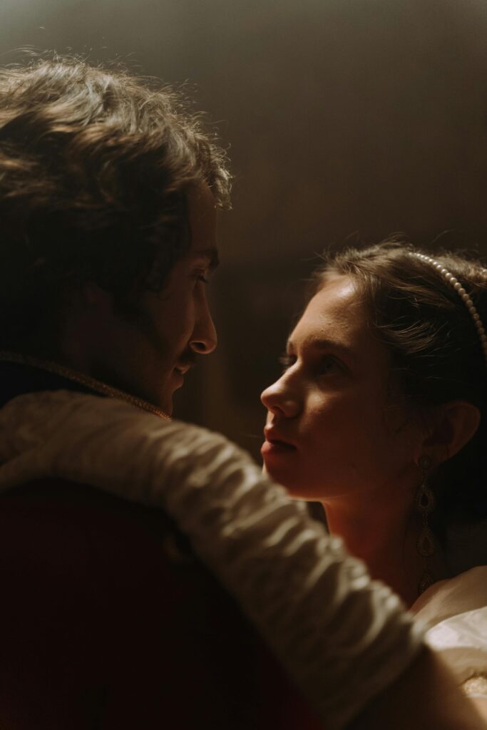 A couple in historical costumes sharing an intimate moment indoors with soft lighting.