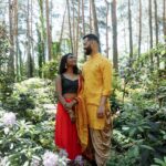 A couple in traditional Indian dress shares a loving moment in a vibrant forest setting.