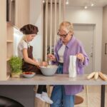 A grandmother and granddaughter joyfully bake at the kitchen counter, bonding over cooking.