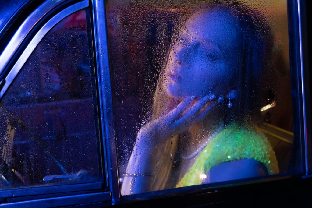 Artistic portrait of a woman through a rain-streaked car window at night.