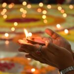 Close-up of a hand holding a lit candle during a religious ceremony surrounded by glowing lights.