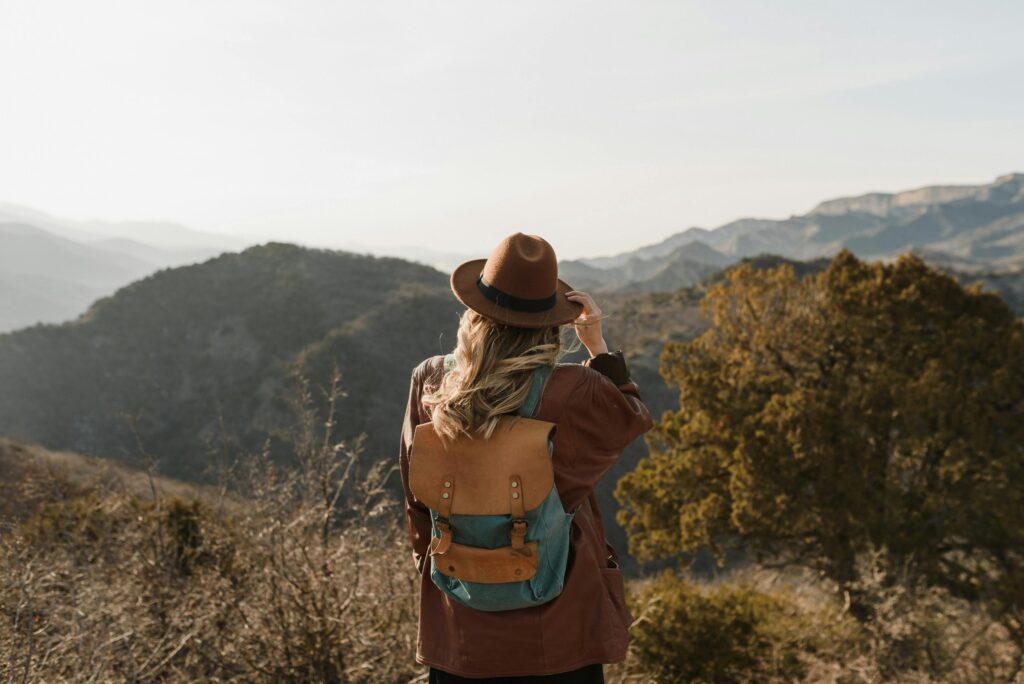 Woman wearing a backpack hiking in mountainous countryside, enjoying the scenic view.