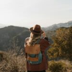 Woman wearing a backpack hiking in mountainous countryside, enjoying the scenic view.