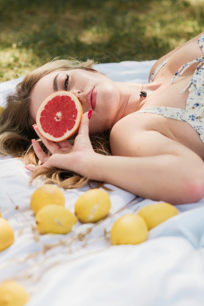 A young woman lying on a picnic blanket holding a sliced grapefruit with lemons around.