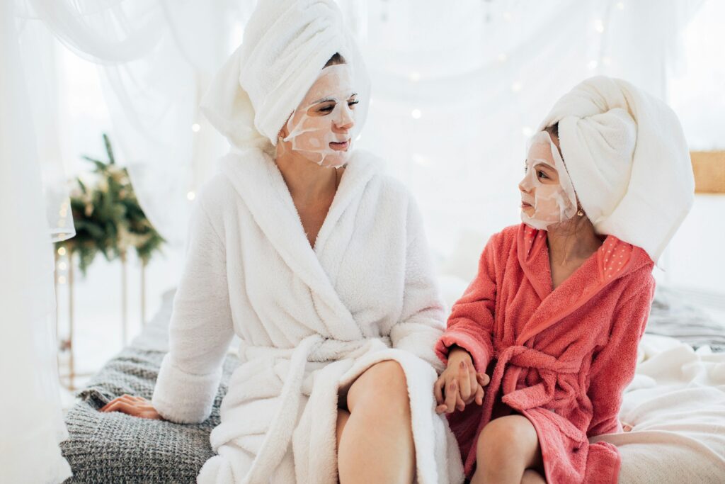 Mother and daughter bonding with face masks and robes, enjoying a spa day at home.