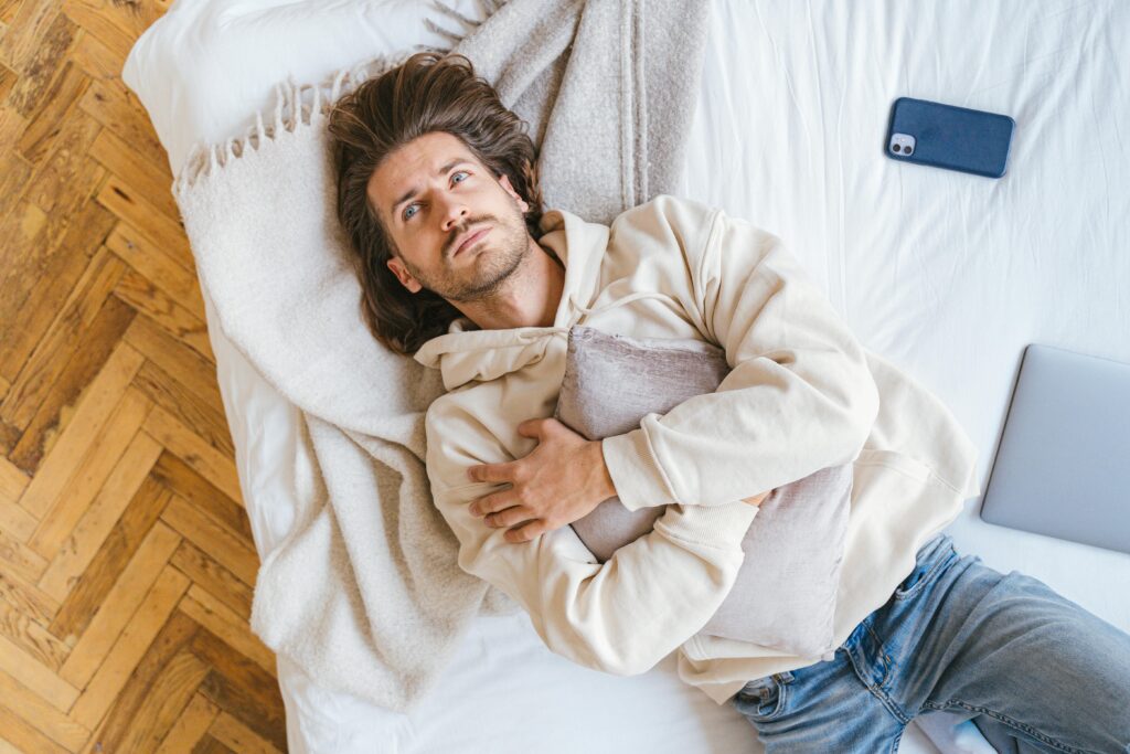 Caucasian man lying on bed hugging a pillow with smartphone nearby, conveying relaxation.
