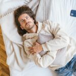 Caucasian man lying on bed hugging a pillow with smartphone nearby, conveying relaxation.