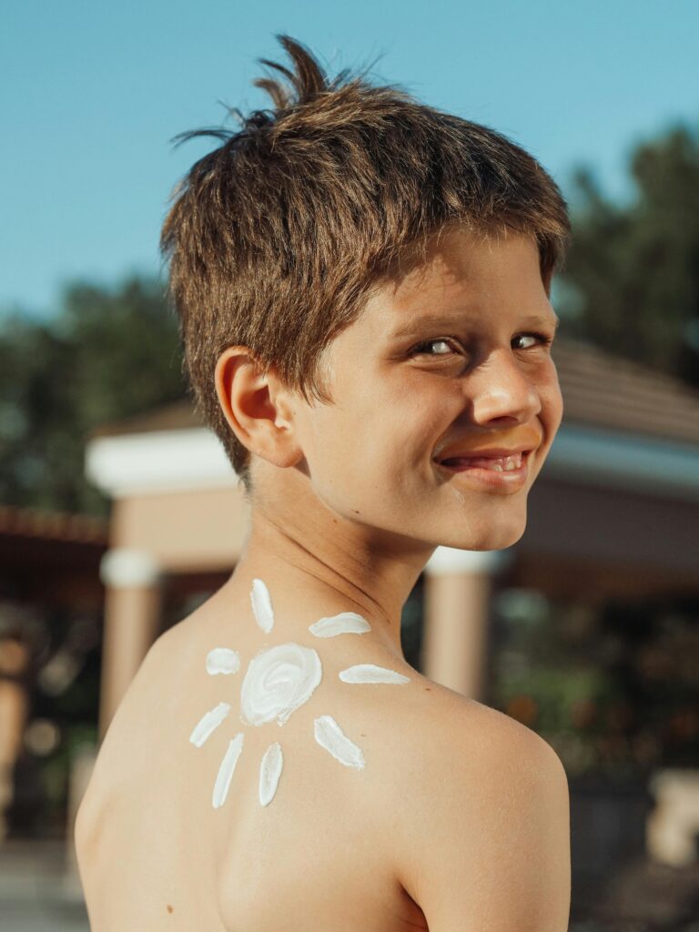 Smiling boy with sunscreen arranged in a sun shape on his back, outdoors.