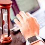 Close-up of a hand on a laptop with an hourglass, symbolizing time management and productivity.