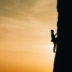 A silhouette of a rock climber scaling a steep cliff during sunset in Russia, showcasing determination and adventure.