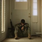 A solitary soldier in uniform sitting by a door, reflecting mood.