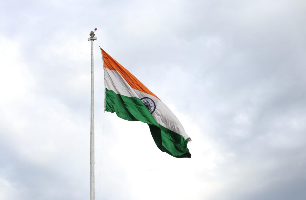 Indian flag waving on a flagpole against a cloudy sky, representing patriotism and national pride.