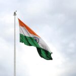Indian flag waving on a flagpole against a cloudy sky, representing patriotism and national pride.