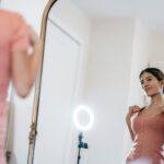 A young woman poses confidently in front of a mirror with a ring lamp.