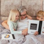 Grandmother reading a storybook with her grandchildren in a cozy bedroom setting, sharing smiles and bonding.