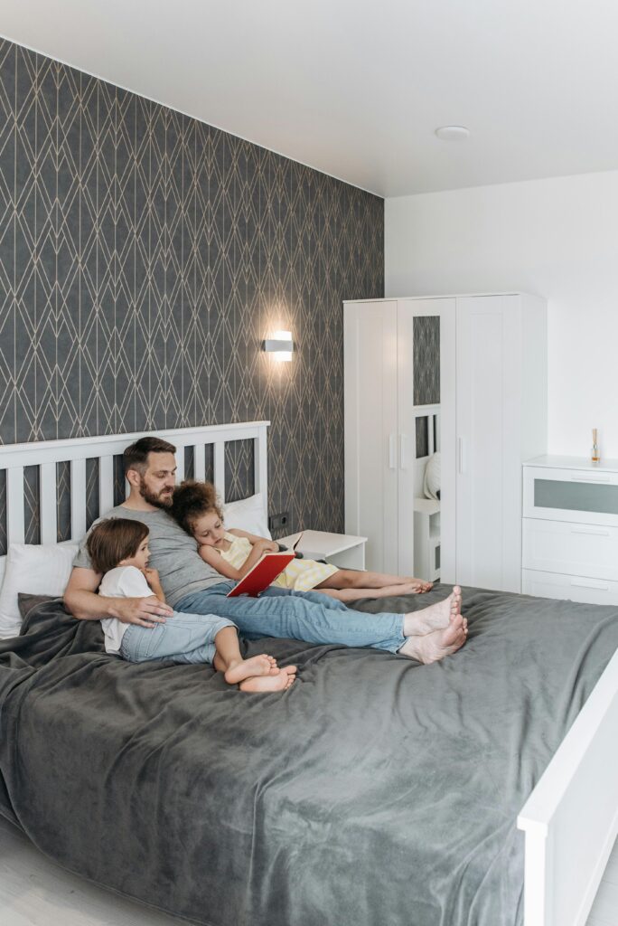 Father reading a book with his children in a comfortable and stylish bedroom setting.