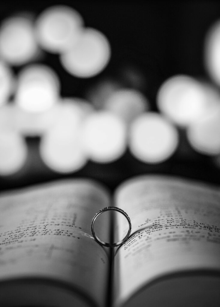 An artistic black and white photo of a ring on an open book page with bokeh background.