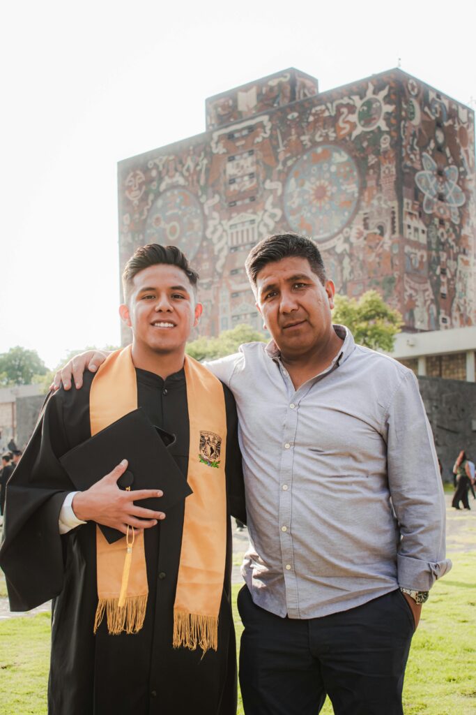 Father and son celebrating graduation in front of UNAM library mural, Mexico City.