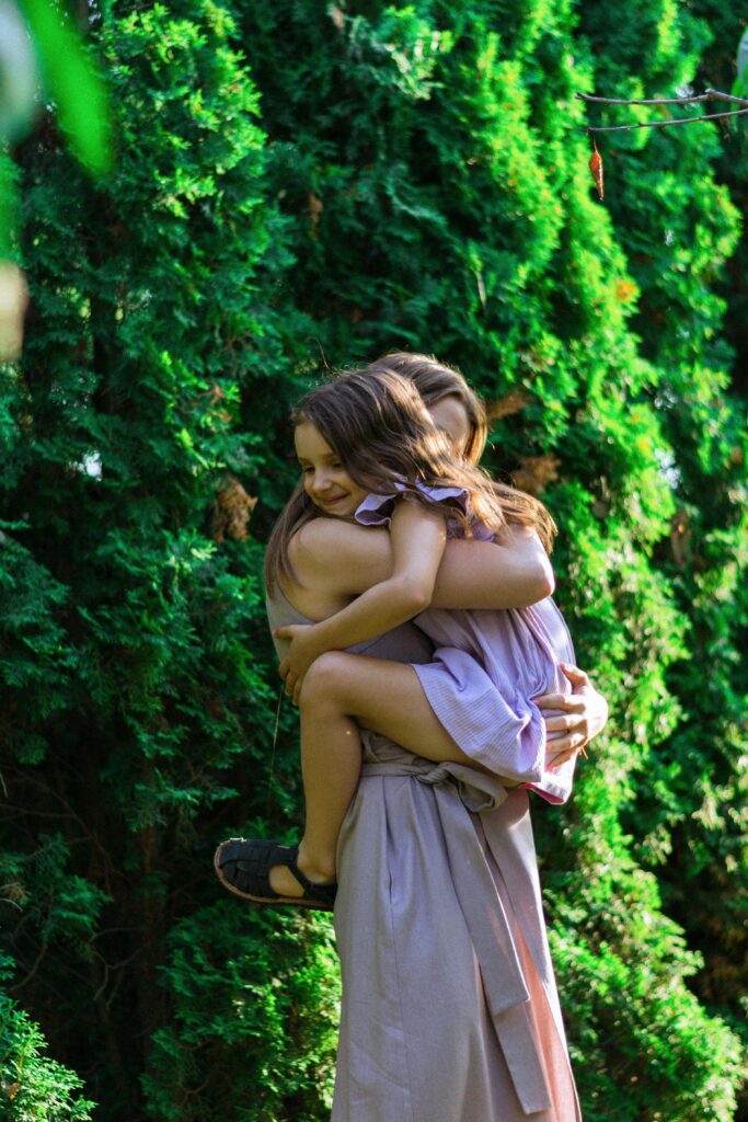 A woman holding and embracing her daughter in a green garden during summer.