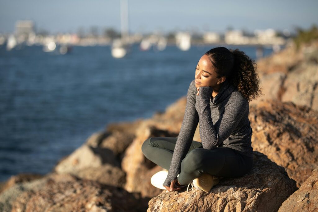 A woman enjoying a peaceful moment sitting on rocks by the seaside, under the sun.