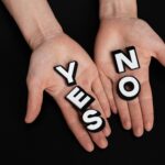 Two hands holding black and white letters spelling 'YES' and 'NO' on a black background.