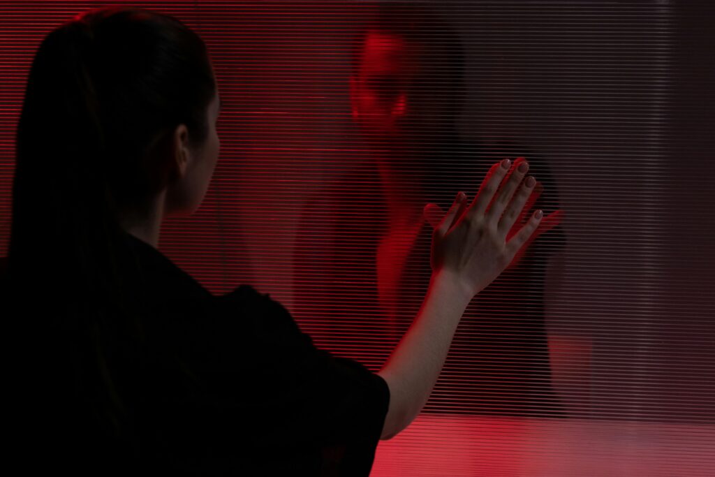 A woman reaches towards her own reflection, illuminated by a dramatic red light.