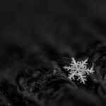 From above black and white of decorative snowflake with pointed edges between thin tangled threads at night