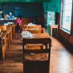 A retro classroom featuring wooden desks, blackboard, and teal walls with a warm ambiance.
