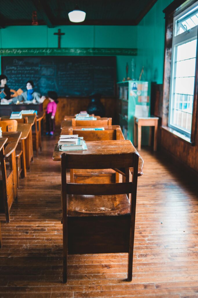 A retro classroom featuring wooden desks, blackboard, and teal walls with a warm ambiance.
