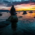 Silhouette of a man seated on rocks, gazing at a serene Lake Tahoe sunset.