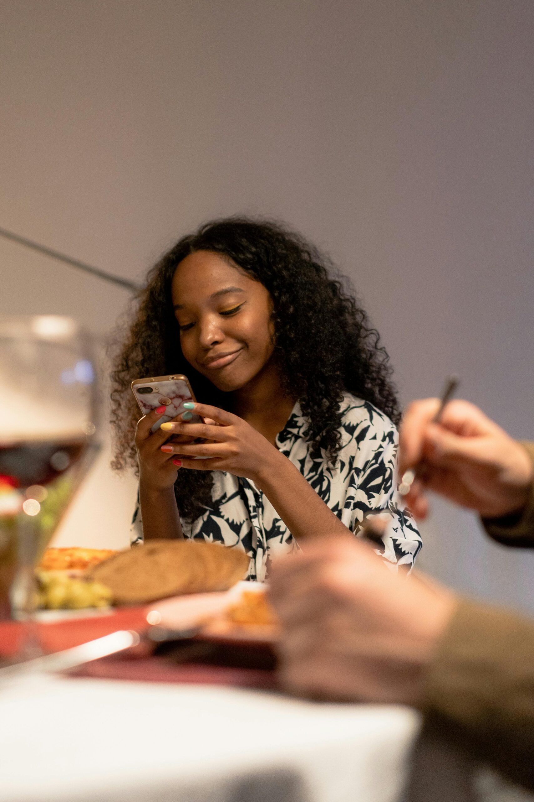 Happy young woman using smartphone while dining with friends indoors.