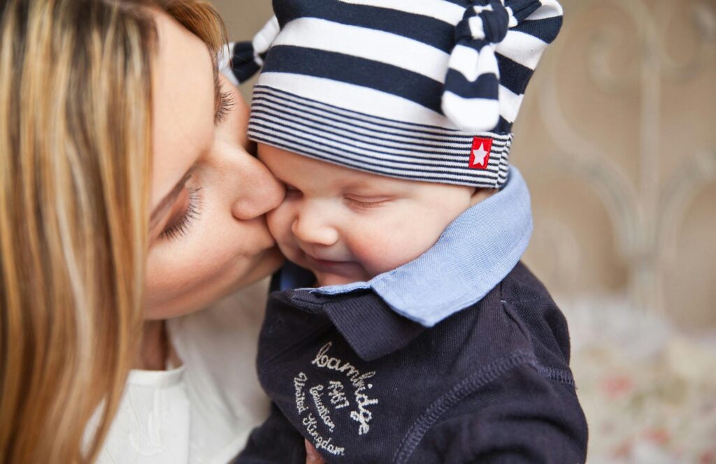 A mother lovingly kisses her smiling baby boy, creating a warm, affectionate scene.