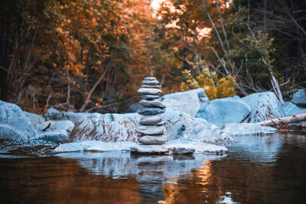Calm forest scene with balanced stones on a riverbed, showcasing vibrant autumn foliage.
