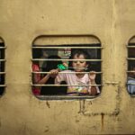 A young child gazes through a barred train window, capturing daily life moments in India.