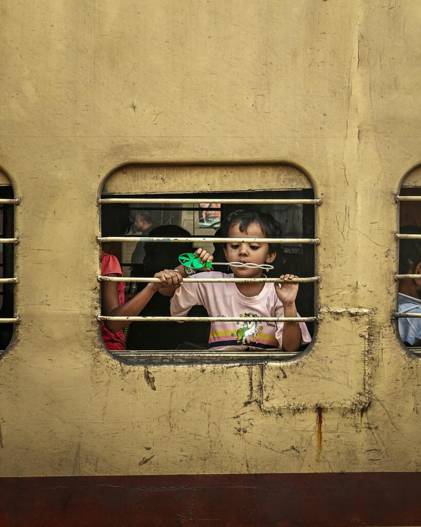 A young child gazes through a barred train window, capturing daily life moments in India.