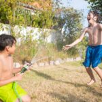 Two children enjoying a playful moment with a garden hose on a sunny day.