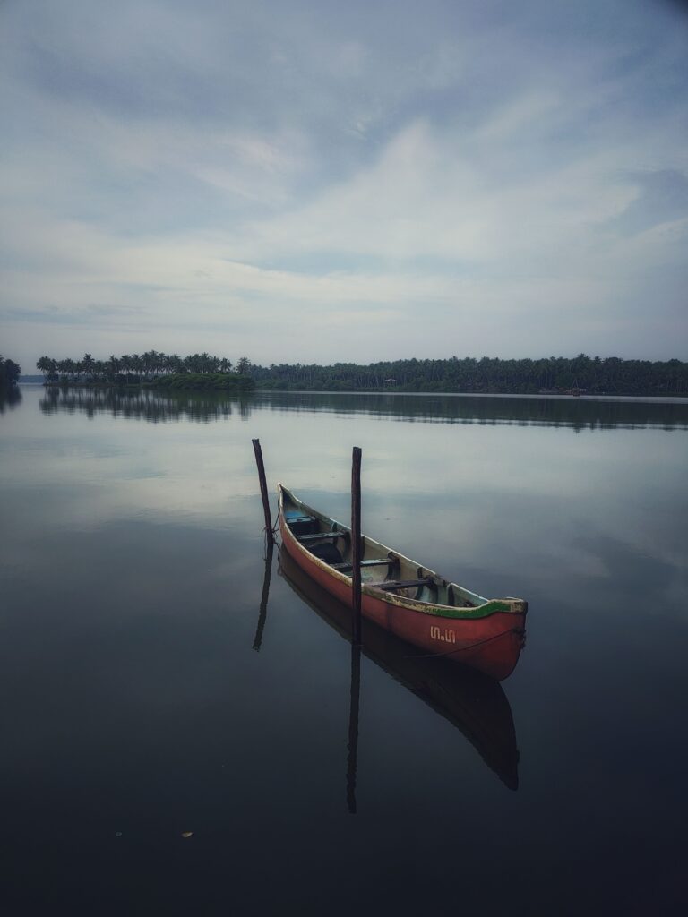 A solitary canoe moored on a peaceful lake in Kerala, India, under a cloudy sky.