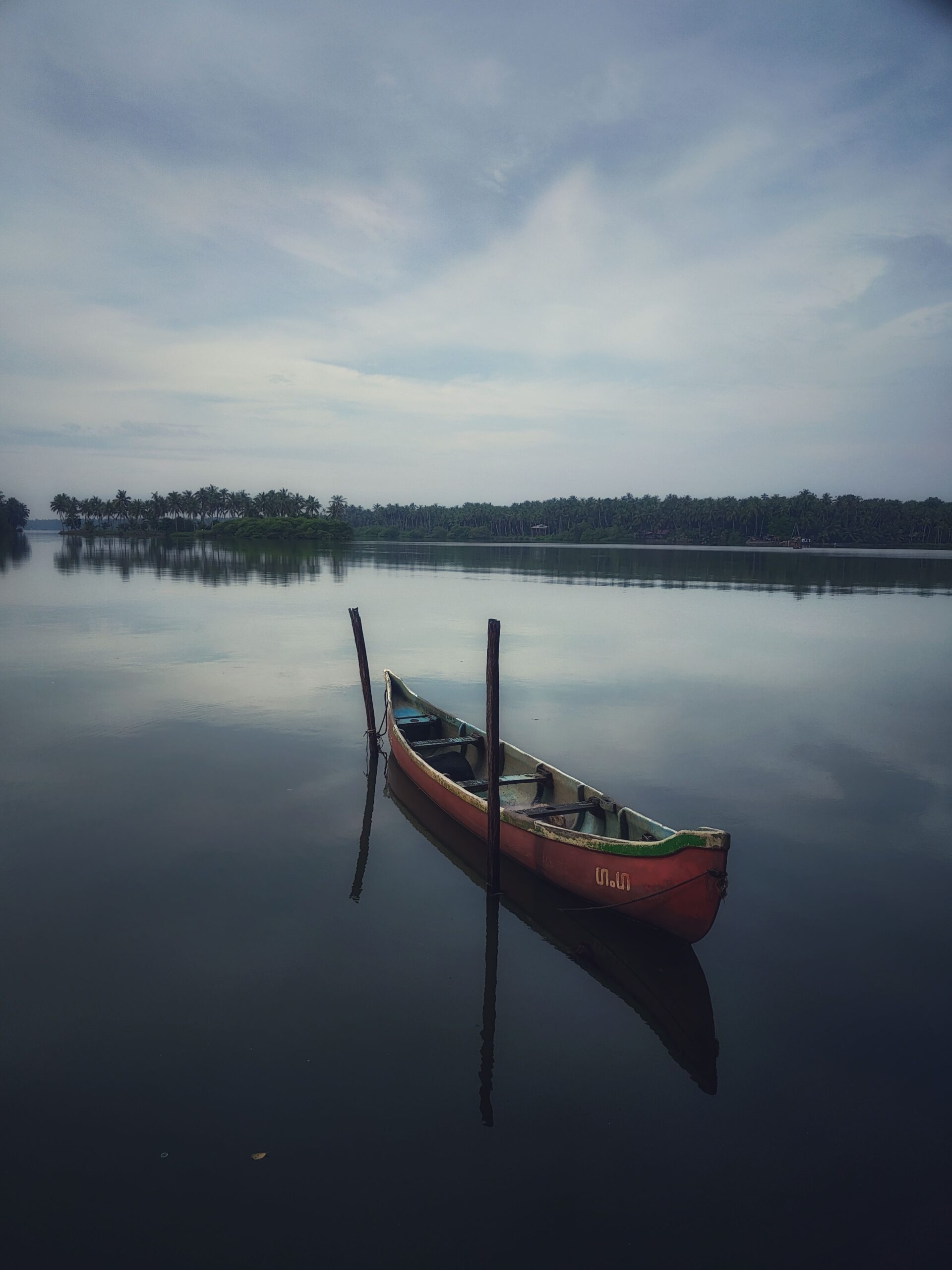 A solitary canoe moored on a peaceful lake in Kerala, India, under a cloudy sky.