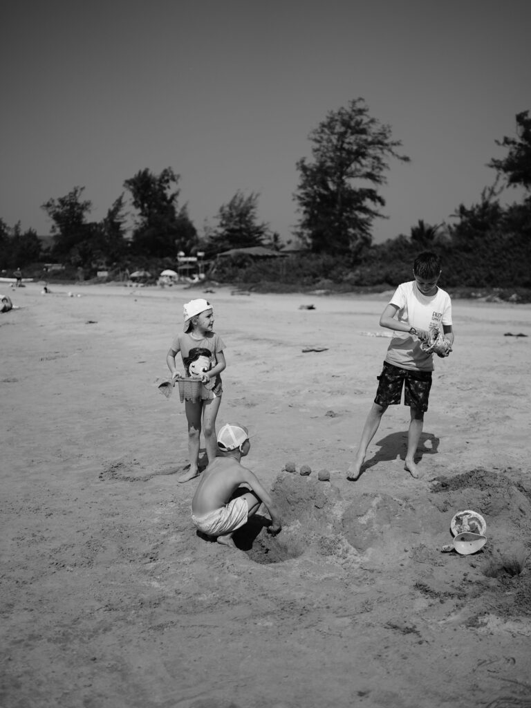 Black and white photo of kids building sandcastles on a Goa beach, India.