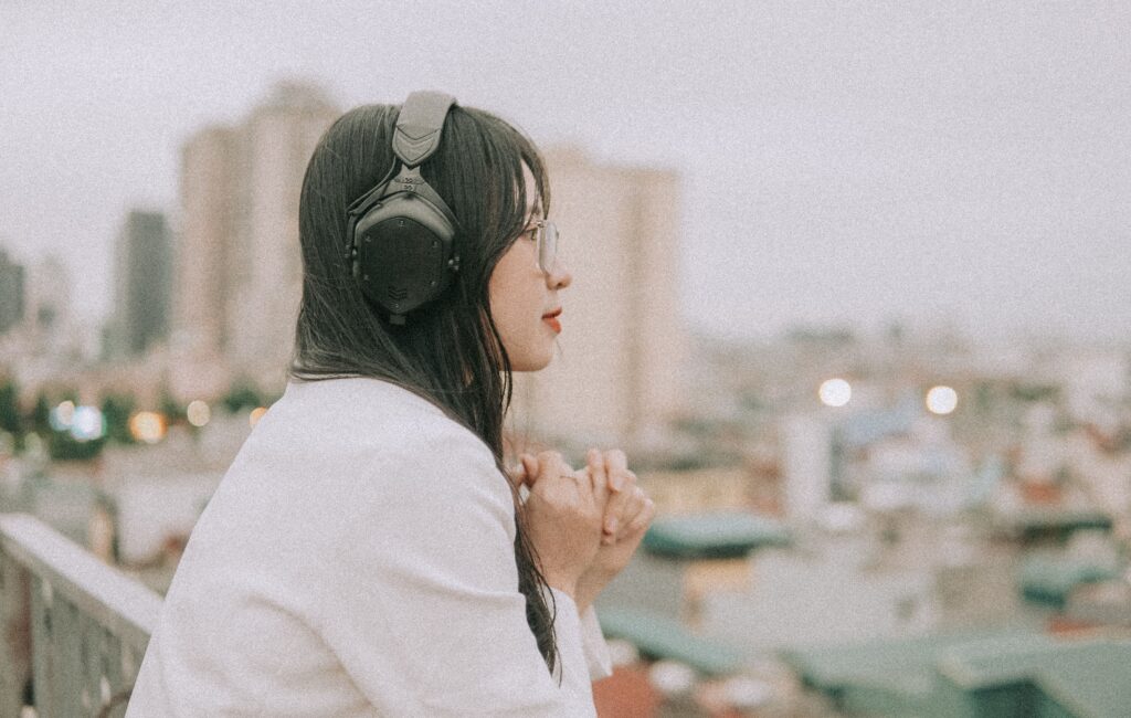 Side view of a woman in headphones and eyeglasses, enjoying a cityscape from a rooftop.